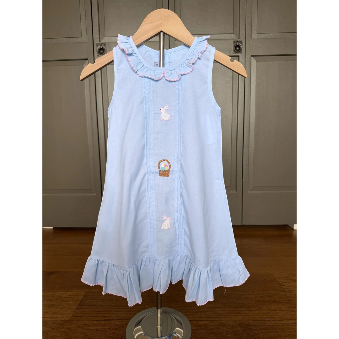 Light blue dress with bunny and carrot design on a wooden hanger against a neutral background