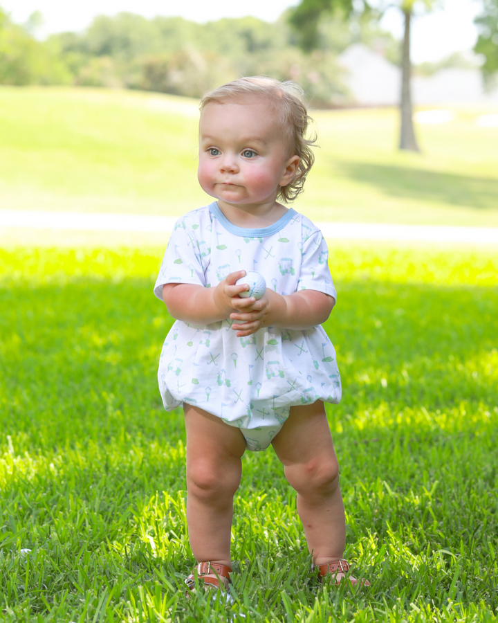 Baby in a light blue outfit standing on grass