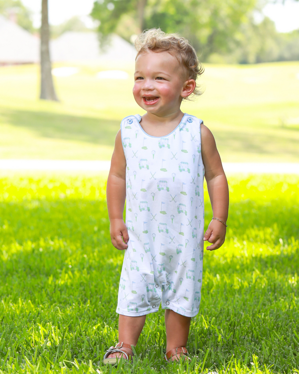 Child wearing a light blue sleeveless dress with a pattern, standing on grass.