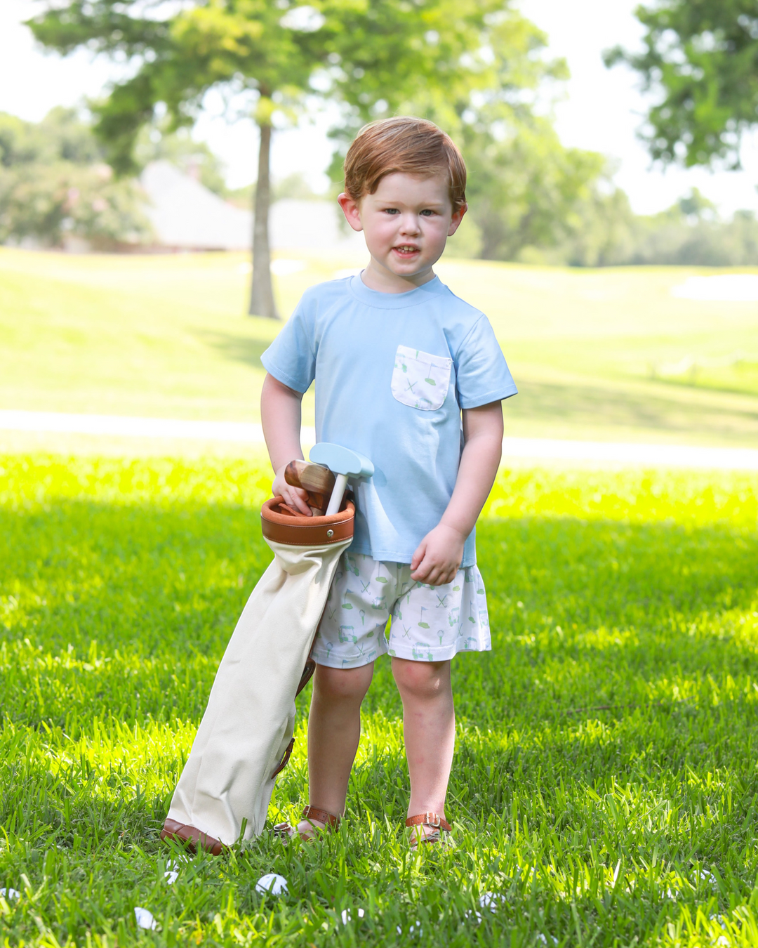 Child standing in a grassy field holding a bag and a wooden object