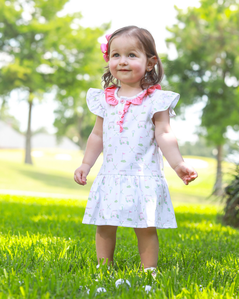 Young girl in a white dress with pink accents standing on grass