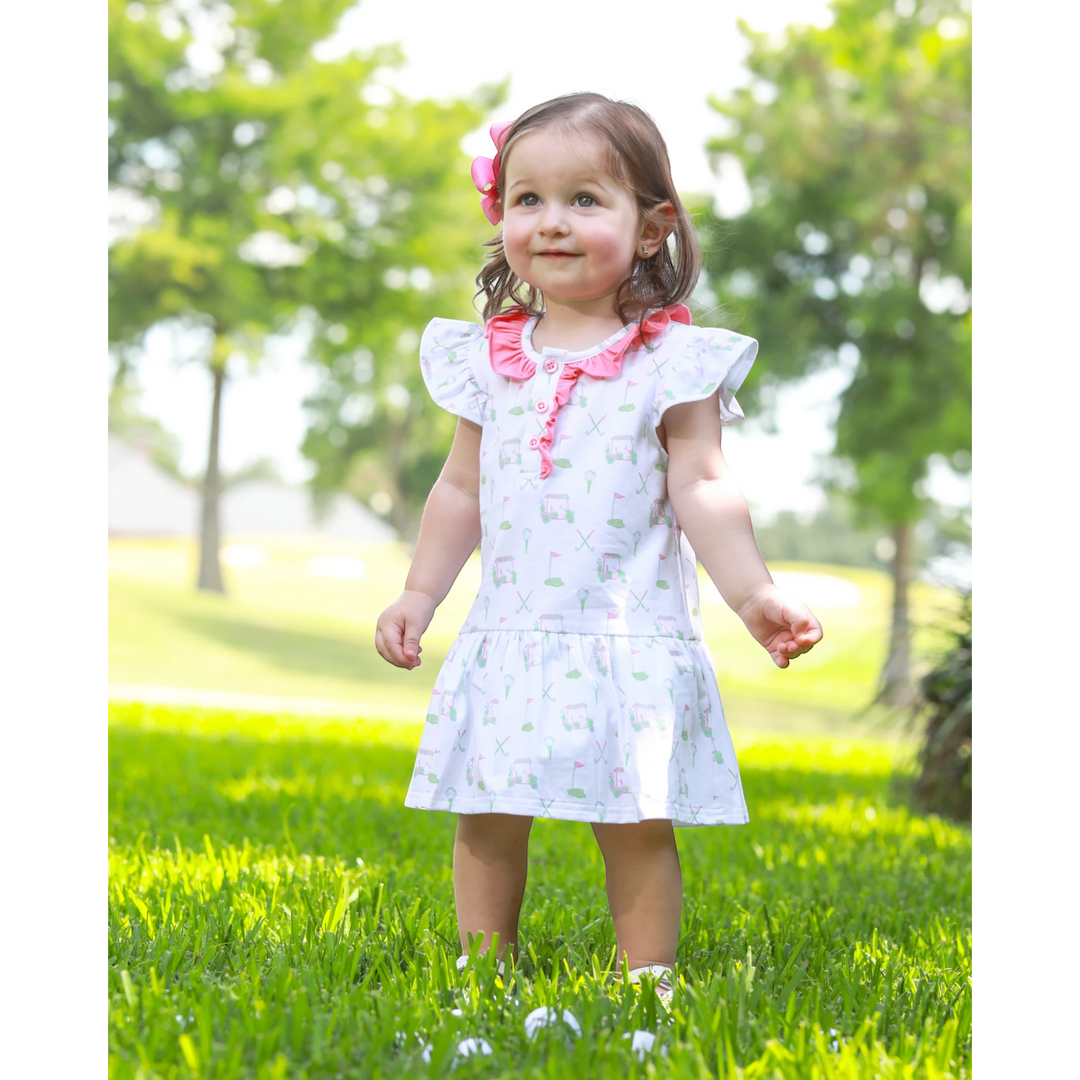 Young girl in a white dress with pink accents standing on grass