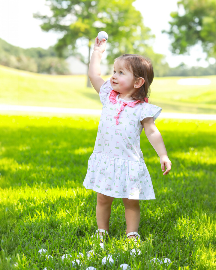 Child in a white dress standing on grass with a white ball in the air
