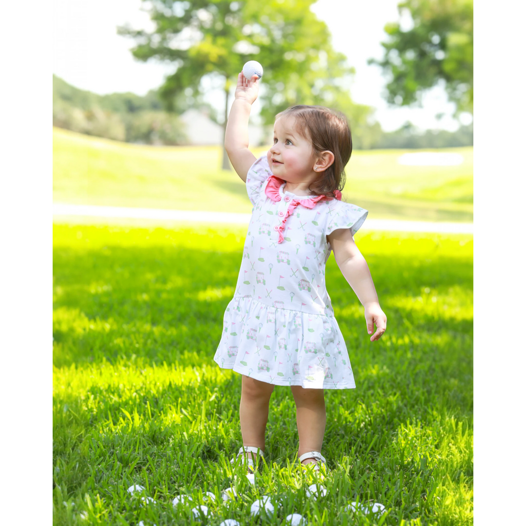 Child in a white dress standing on grass with a white ball in the air