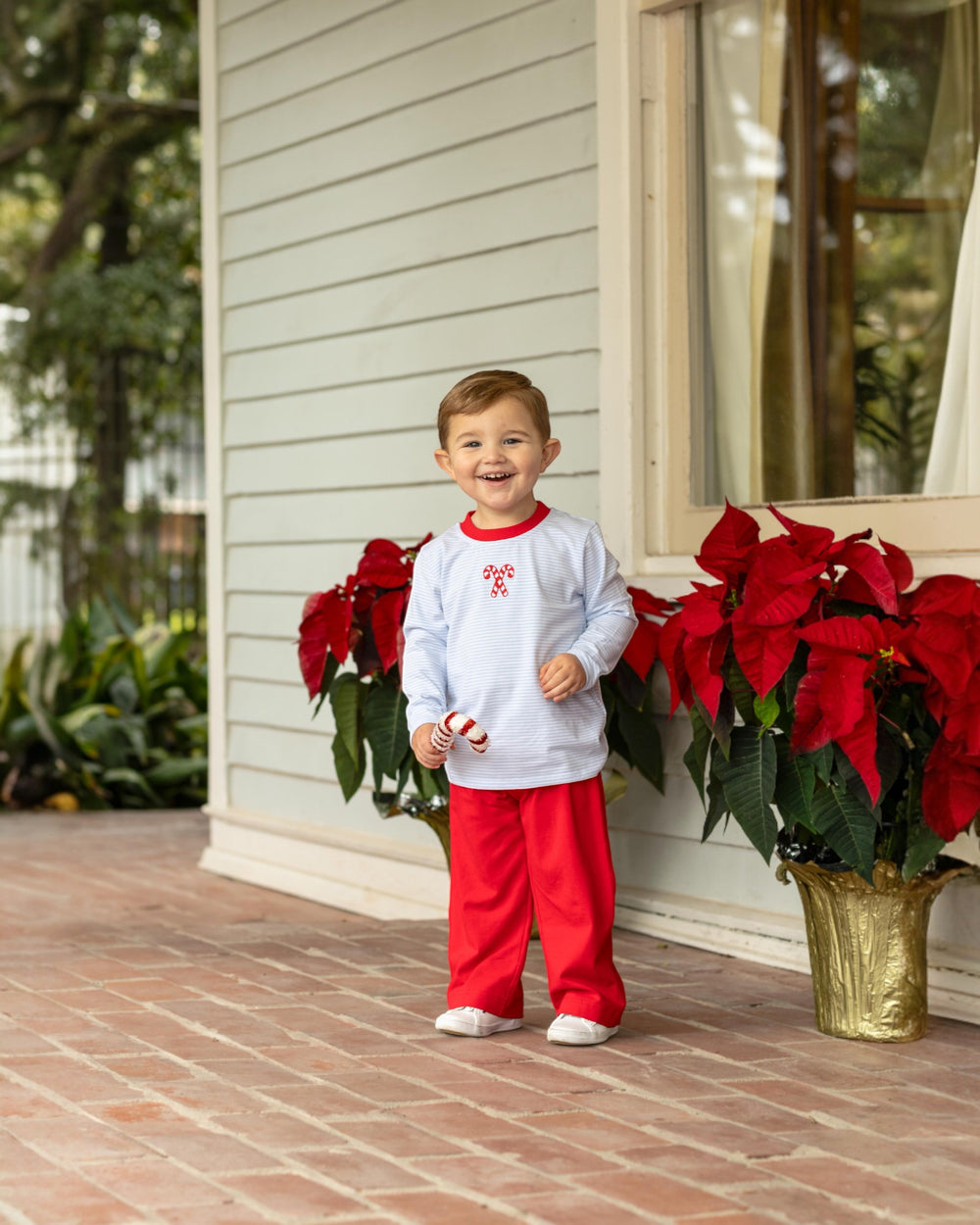 Child in red and white outfit standing on a porch with poinsettias
