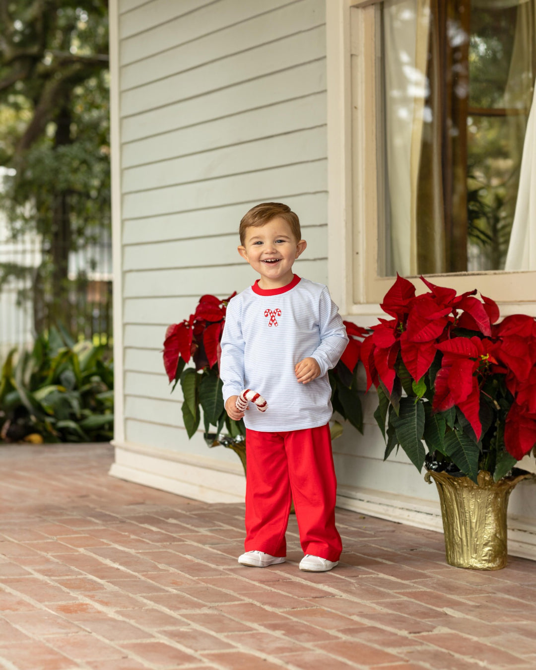 Child in red and white outfit standing on a porch with poinsettias