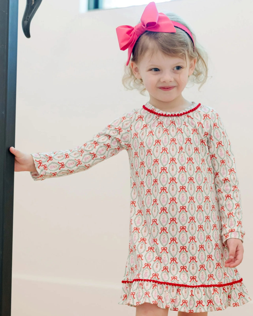 Child wearing a patterned dress with a pink bow headband against a white background