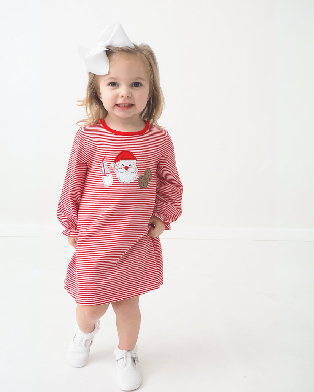 Child wearing a red and white striped dress with a Santa Claus design on a white background