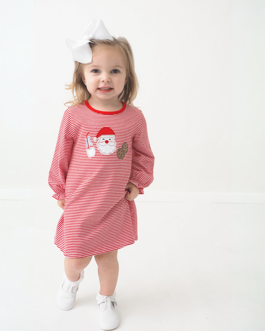 Child wearing a red and white striped dress with a Santa Claus design on a white background