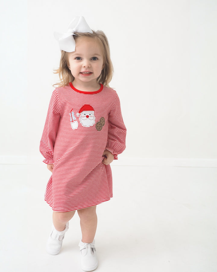 Child wearing a red and white striped dress with a Santa Claus design on a white background