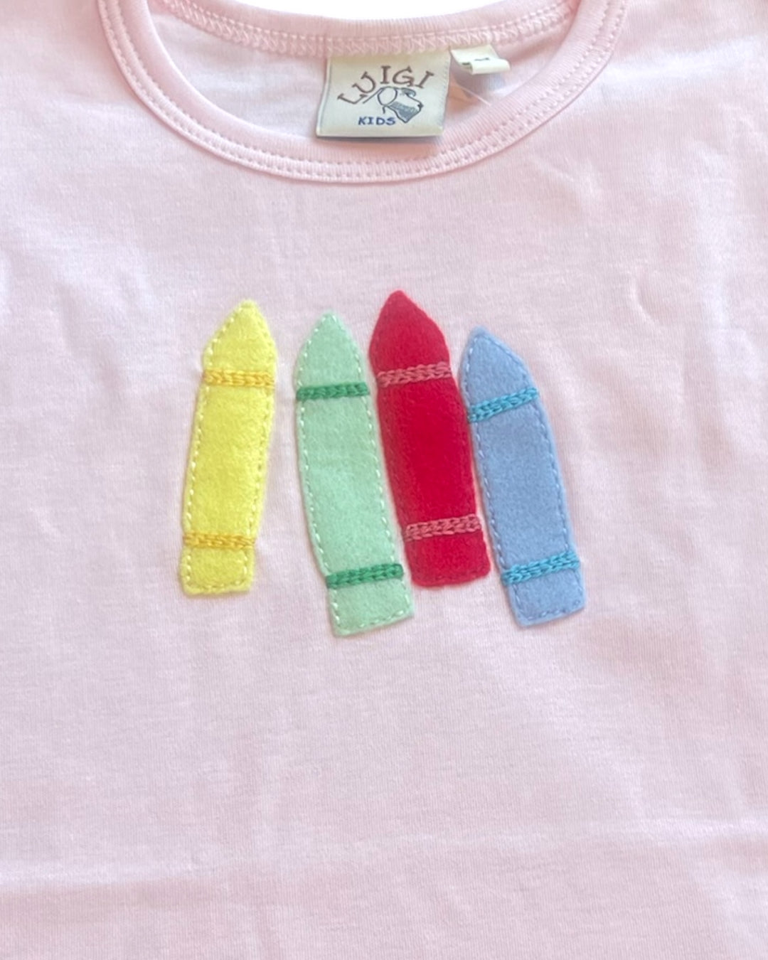 Pink shirt with colorful crayon-shaped appliqués on a white background