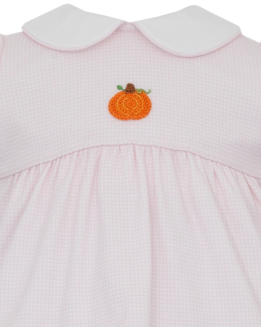 Close-up of a light pink gingham dress with a white Peter Pan collar and an orange pumpkin applique on the chest, that store