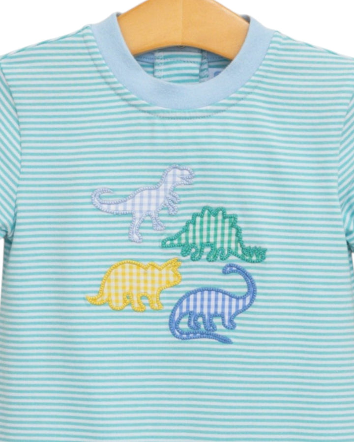 A close-up of a baby or toddler long-sleeve shirt with light blue and white horizontal stripes, featuring four embroidered dinosaur motifs in pastel colors (purple, green, yellow, and blue) on the front, hanging on a wooden hanger, that store