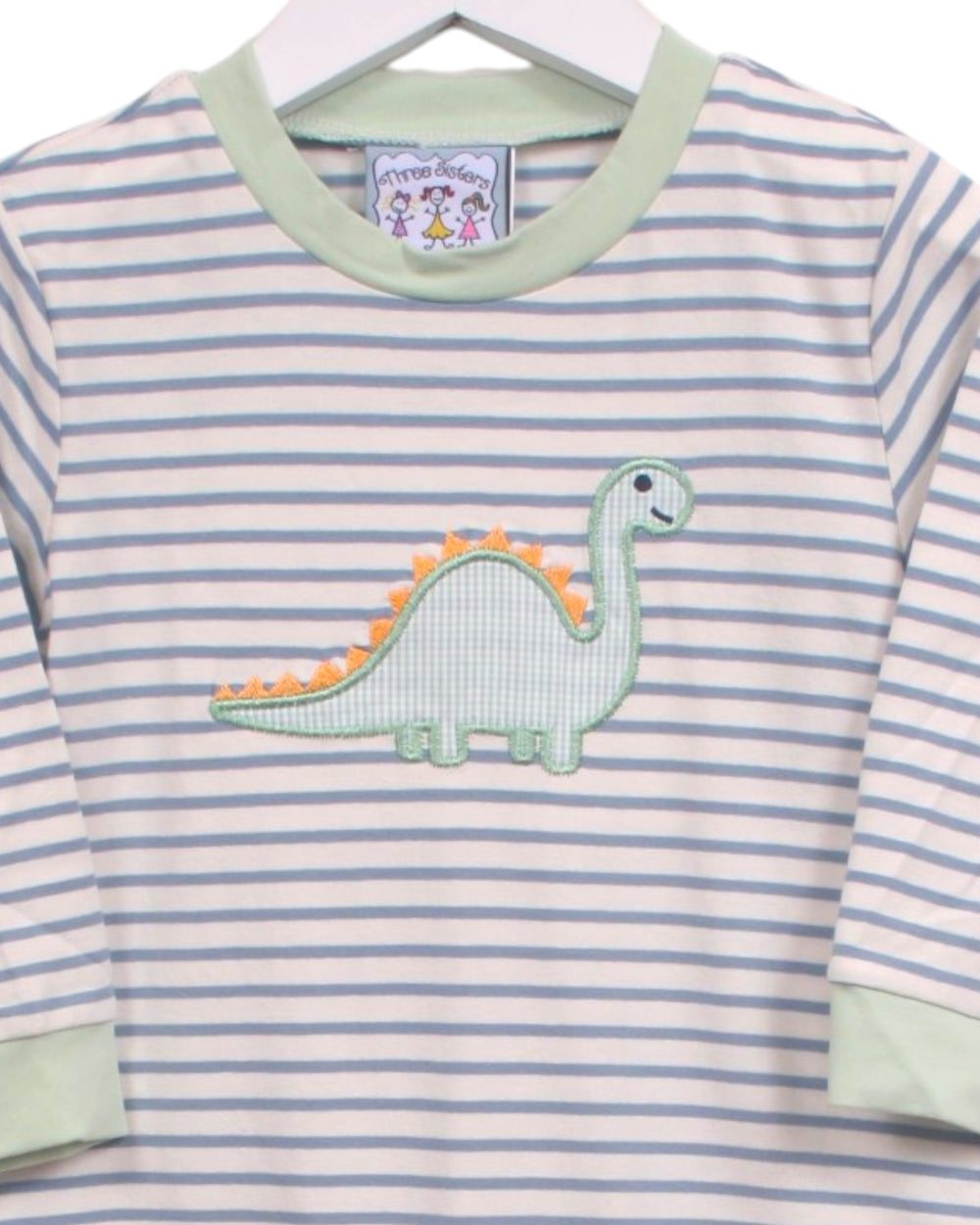 A baby long-sleeve shirt with light blue and white horizontal stripes, featuring a light green crew neck, light green cuffs, and an applique of a green and orange dinosaur on the chest. The shirt is hanging on a white hanger, that store