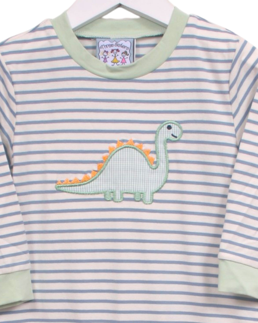 A baby long-sleeve shirt with light blue and white horizontal stripes, featuring a light green crew neck, light green cuffs, and an applique of a green and orange dinosaur on the chest. The shirt is hanging on a white hanger, that store