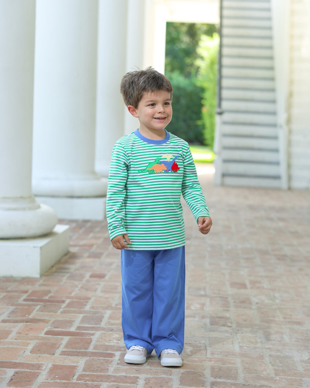 Child wearing a green and blue striped shirt with a colorful design outdoors.
