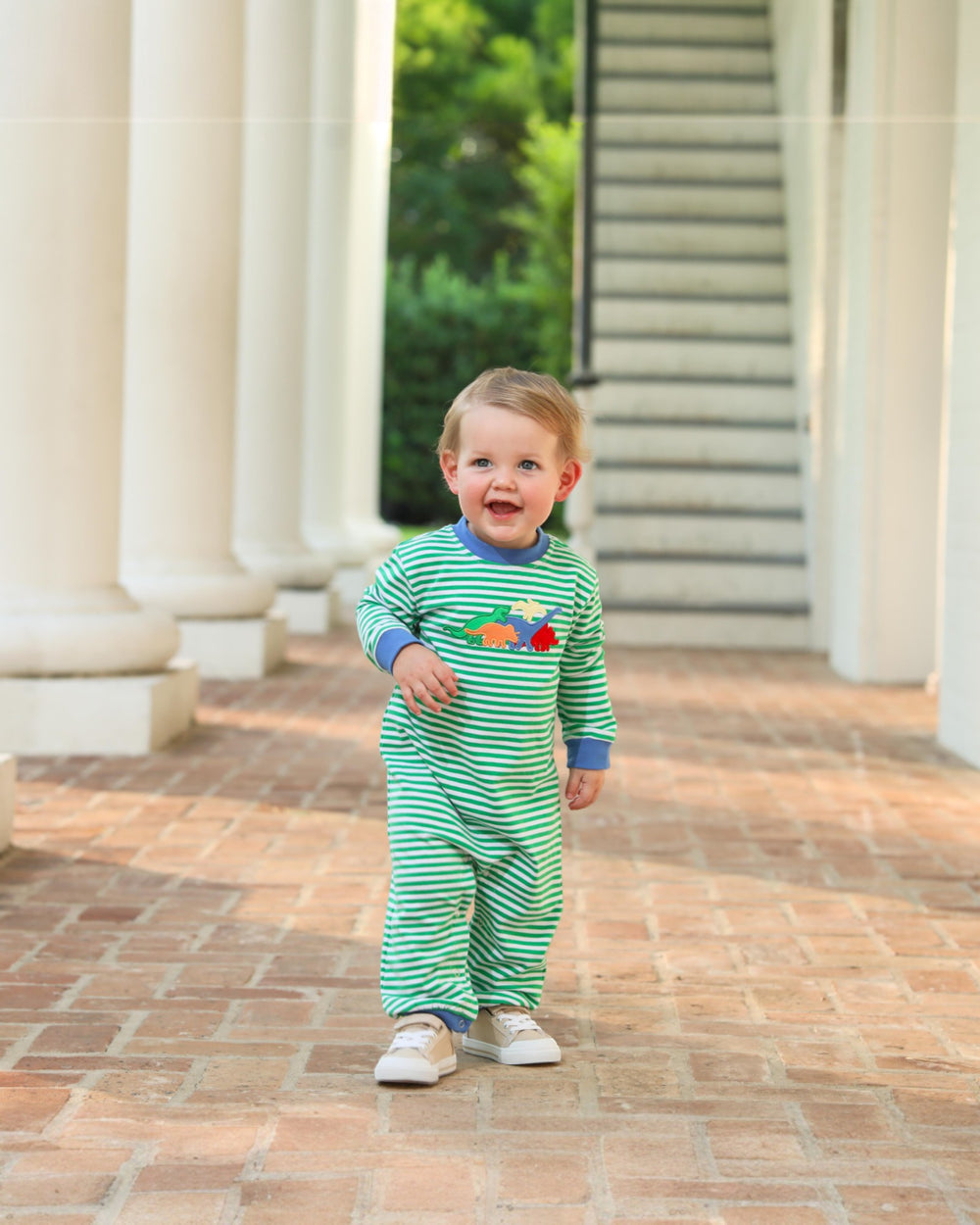 Child wearing a green and white striped outfit with colorful characters, standing on a brick path.