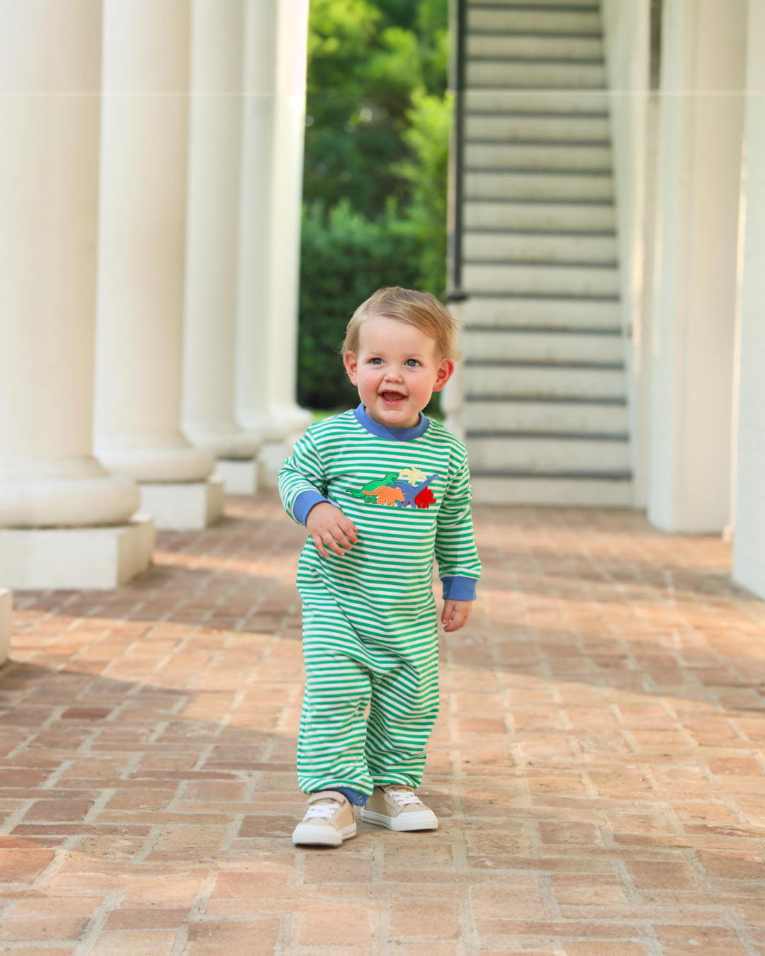 Child wearing a green and white striped outfit with colorful characters, standing on a brick path.