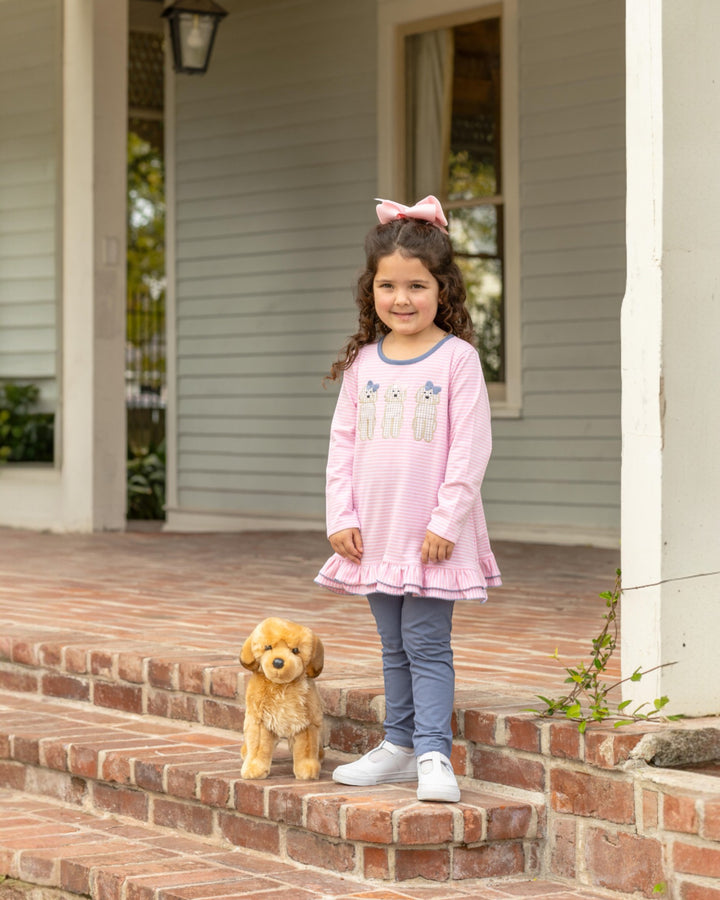 Young girl in a pink dress standing on a porch with a small dog.