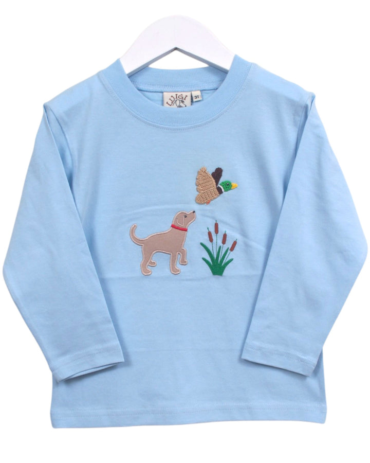 A light blue long-sleeve baby t-shirt on a white hanger, featuring embroidered graphics of a tan dog, a duck, and green reeds on the front, that store