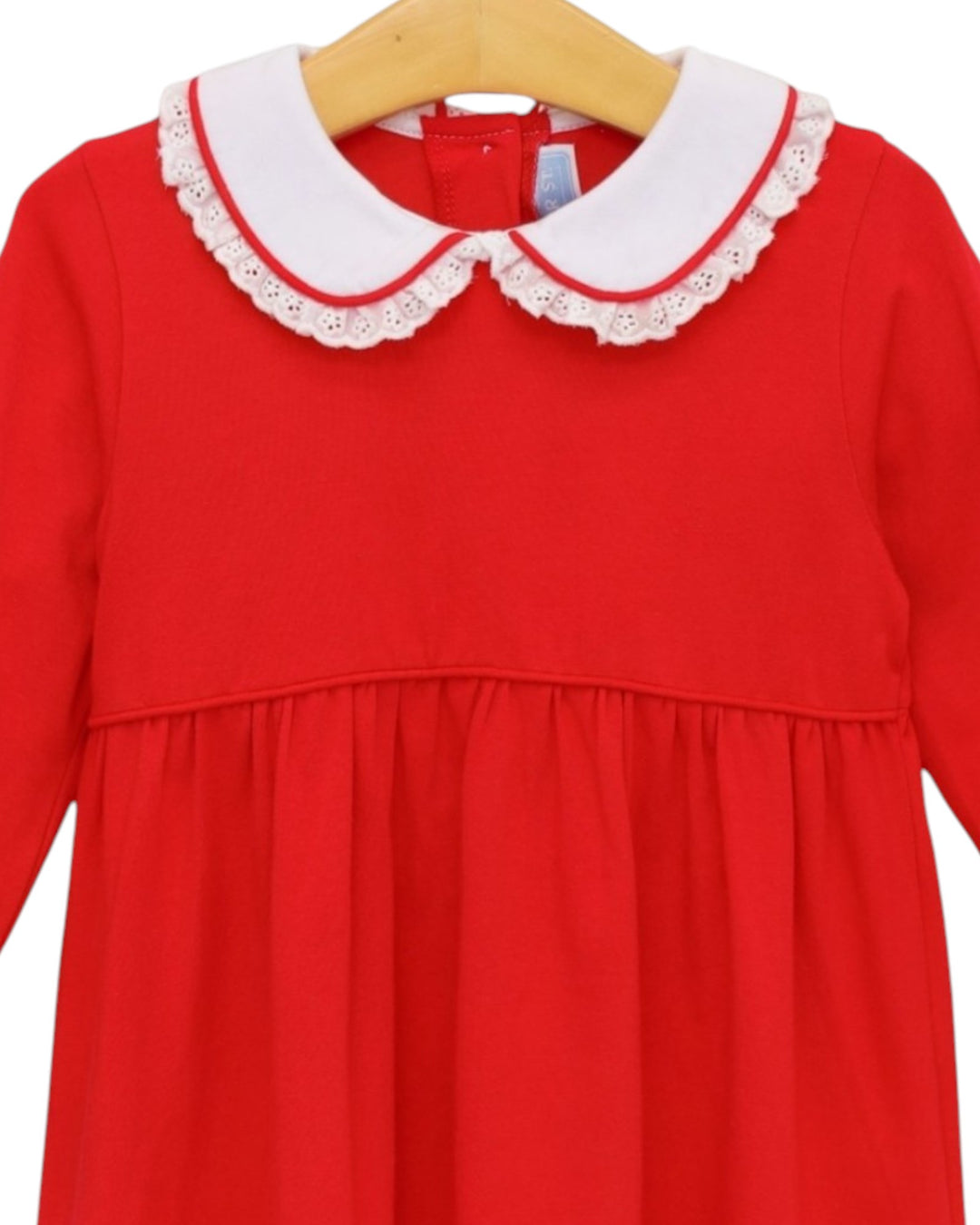 A bright red long-sleeve dress with a white eyelet Peter Pan collar, hanging on a wooden hanger against a white background, that store