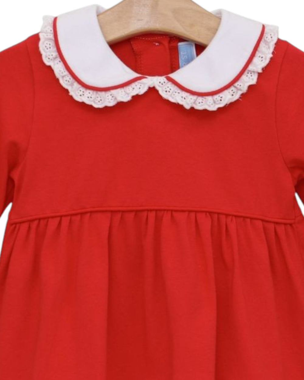 A red children's dress hanging on a wooden hanger, featuring a white Peter Pan collar with red trim and white eyelet lace, that store