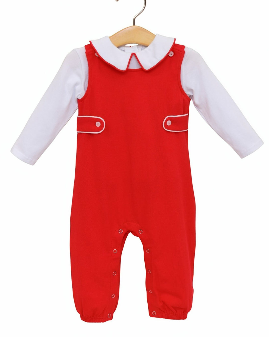 A baby red overall jumpsuit with a white long-sleeve shirt underneath, displayed on a wooden hanger against a plain white background, that store