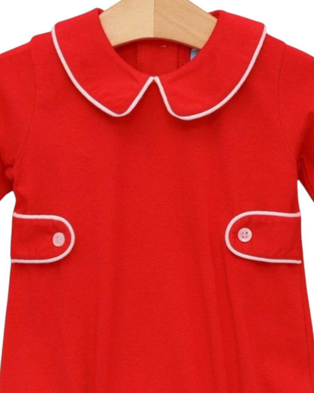 A bright red children's dress with a white-trimmed Peter Pan collar and matching white piping details on the chest pockets, hanging on a wooden hanger against a white background, that store