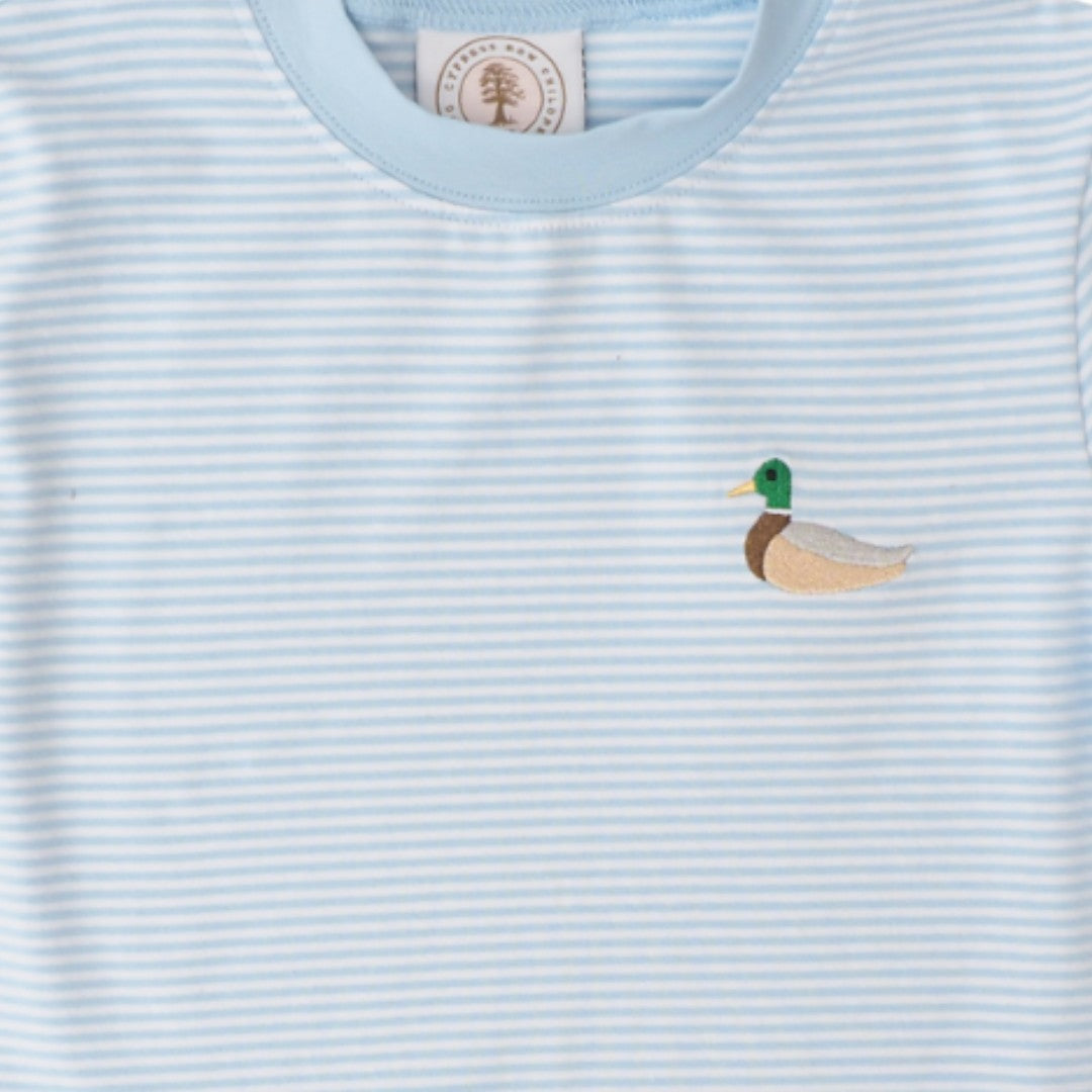 A close-up of a light blue and white striped baby t-shirt featuring a small embroidered mallard duck on the left chest. The inner neck label shows a circular logo with a tree and the text &