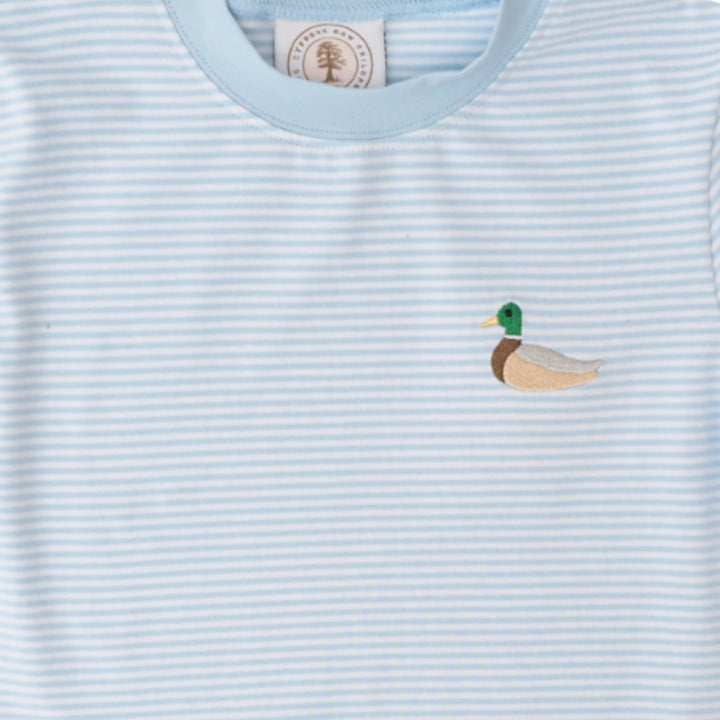 A close-up of a light blue and white striped baby t-shirt featuring a small embroidered mallard duck on the left chest. The inner neck label shows a circular logo with a tree and the text &