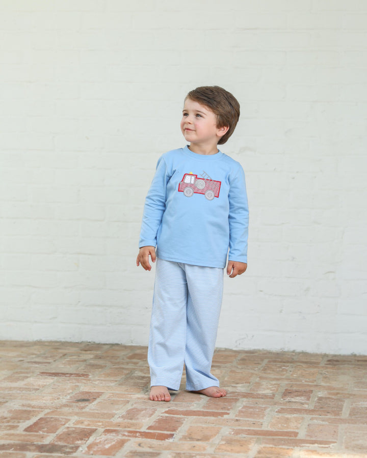 Child wearing a light blue pajama set with a red truck design on a white brick floor.