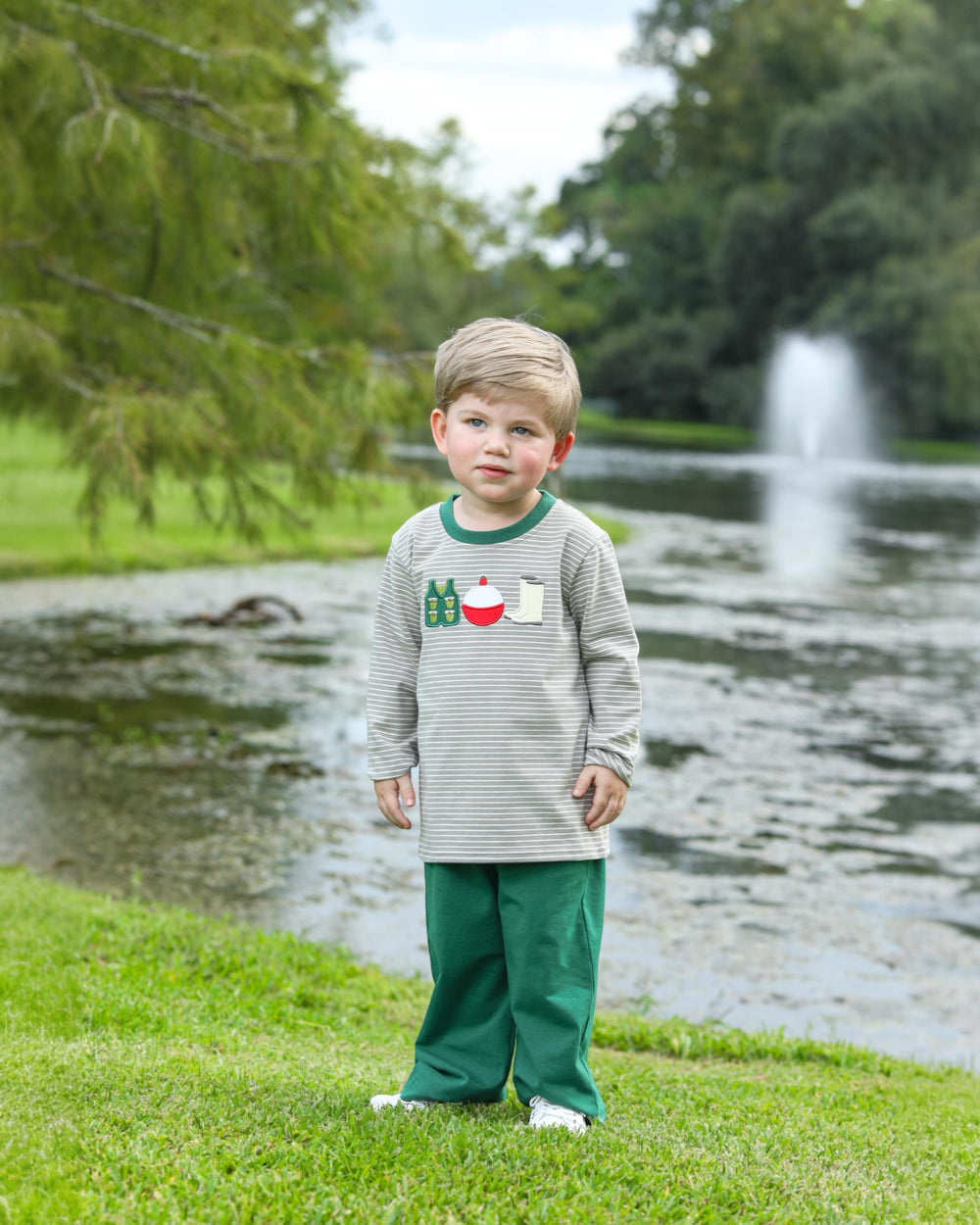 Child wearing a sweater with cartoon designs by a pond