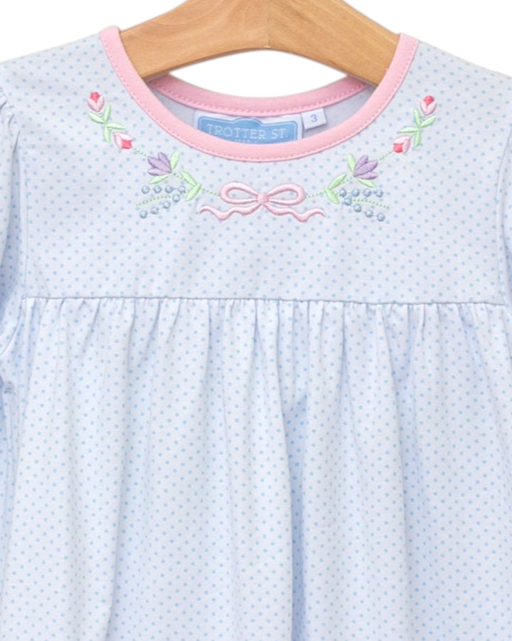 Light blue dress with pink trim and floral embroidery on a wooden hanger.