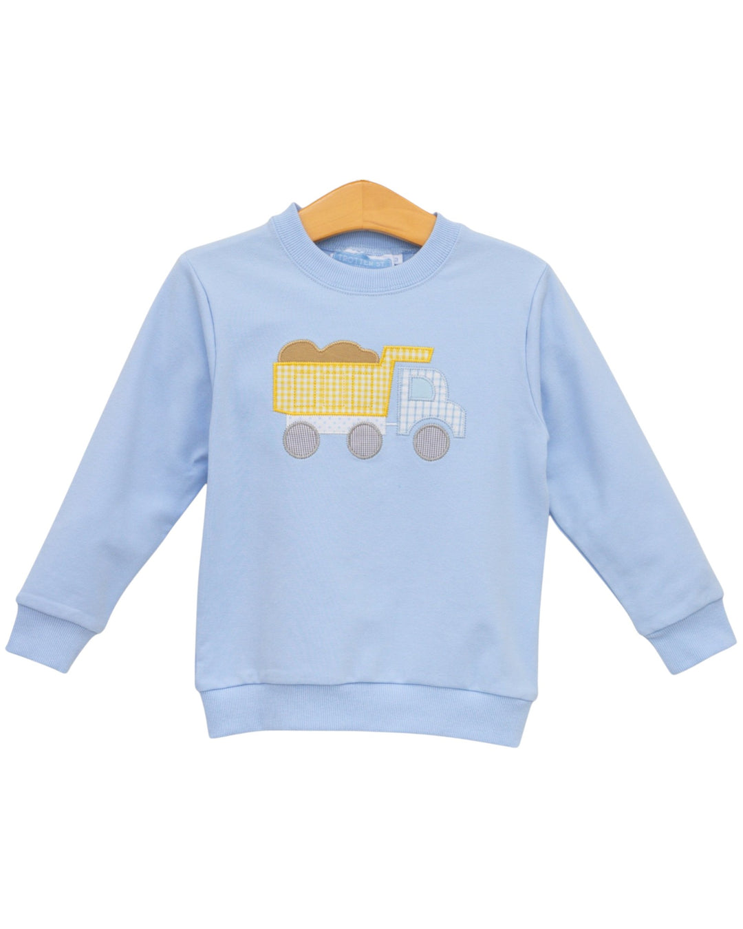 A light blue long-sleeve crewneck sweatshirt for toddlers, featuring a yellow and white checkered dump truck applique on the chest, displayed on a wooden hanger against a white background, that store