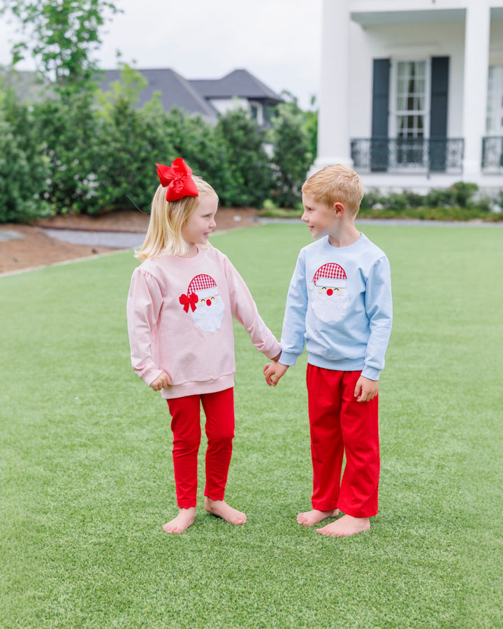 Two children holding hands on a grassy lawn wearing matching outfits with red and blue designs.