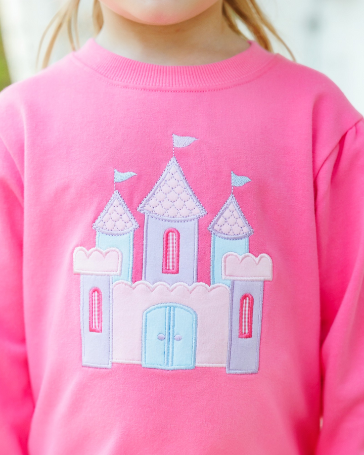 A close-up of a child wearing a bright pink crewneck sweatshirt with a light blue and lavender embroidered castle design on the front, that store