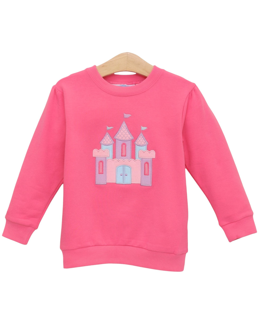 A pink long-sleeve crewneck sweatshirt for kids, featuring a light blue and lavender castle graphic on the front, displayed on a wooden hanger against a white background, that store