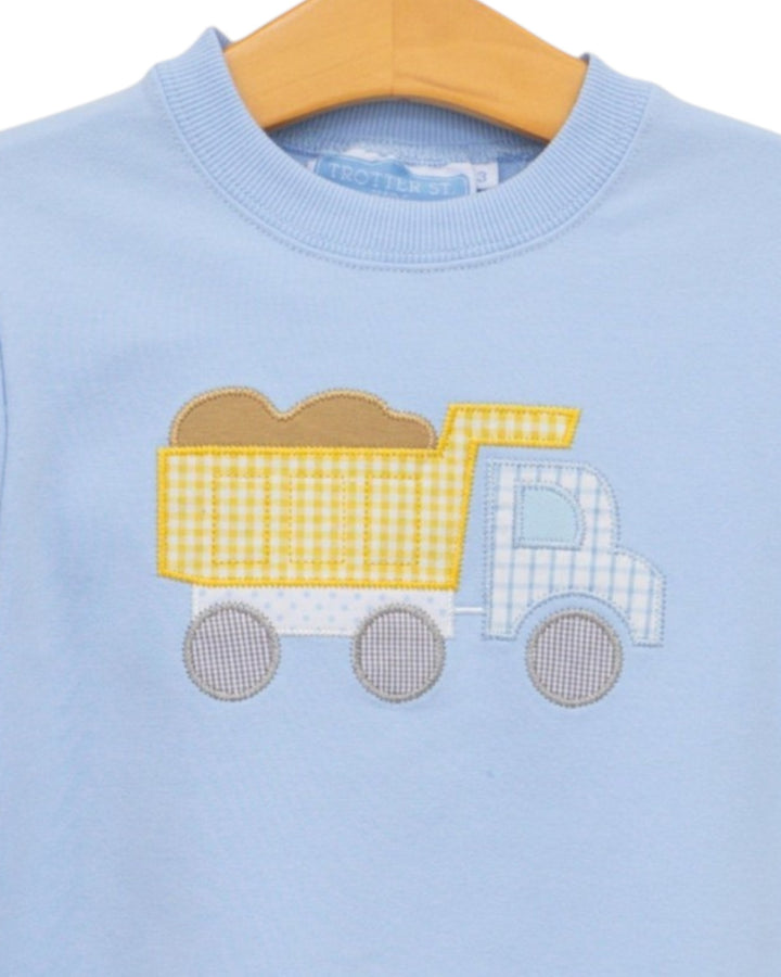 A light blue crewneck sweatshirt on a wooden hanger, featuring an applique design of a dump truck with a yellow and white gingham patterned body, brown cargo, and gray wheels, that store
