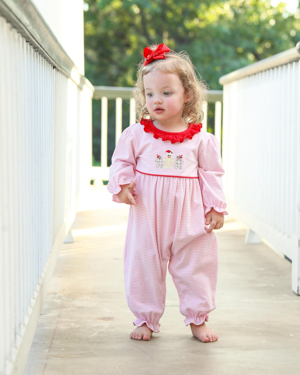Child wearing a pink outfit with red trim on a wooden deck