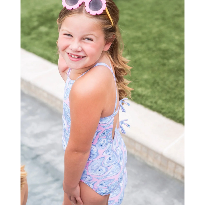 Young girl in a colorful swimsuit standing by a poolside.