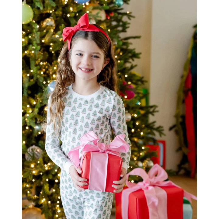 Young girl holding a gift box with a pink bow in front of a decorated Christmas tree.