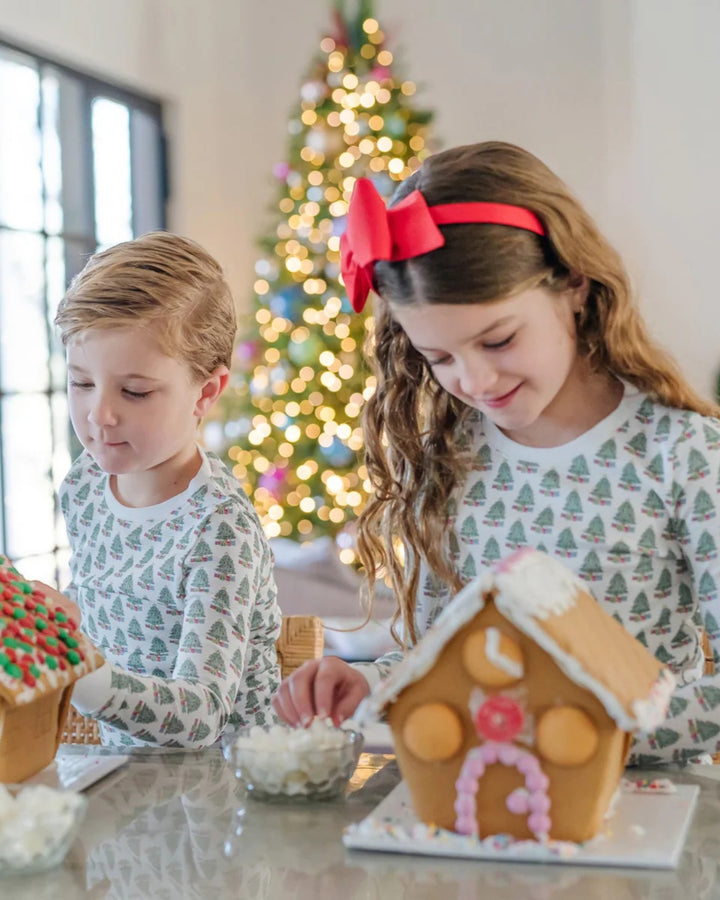 Two children decorating gingerbread houses with a Christmas tree in the background.