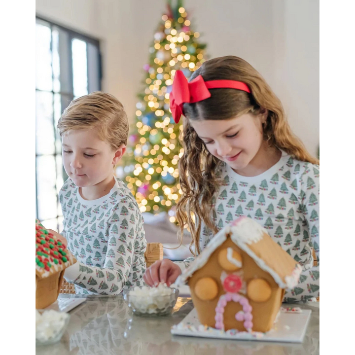 Two children decorating gingerbread houses with a Christmas tree in the background.
