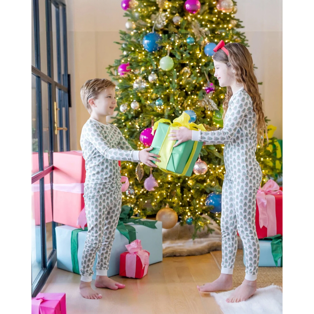 Two children in matching pajamas exchanging gifts in front of a decorated Christmas tree.
