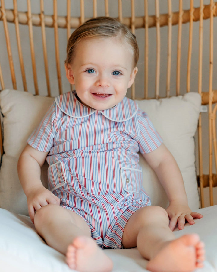 Baby wearing a striped romper sitting on a cushioned chair.