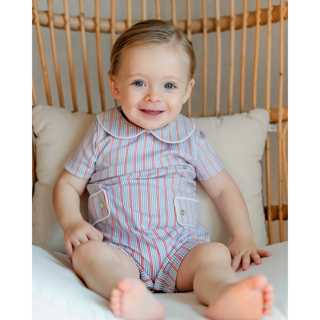 Baby wearing a striped romper sitting on a cushioned chair.