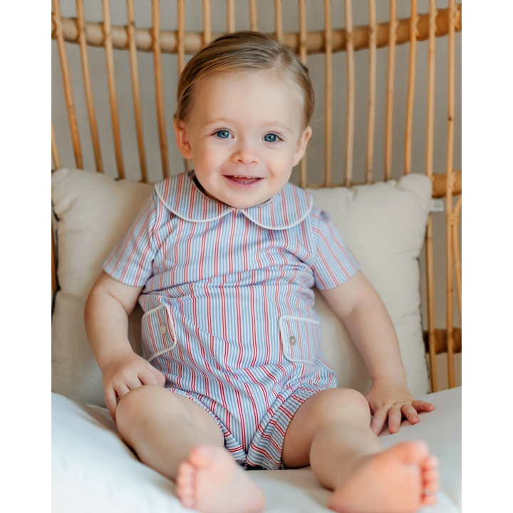 Baby wearing a striped romper sitting on a cushioned chair.