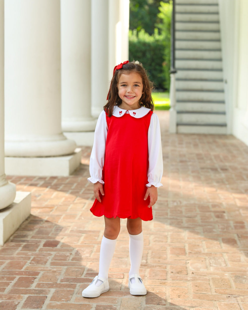 Young girl in a red dress and white shirt standing on a brick path.