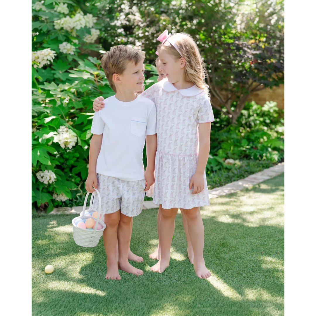 Two children standing outdoors in a garden with greenery and flowers.