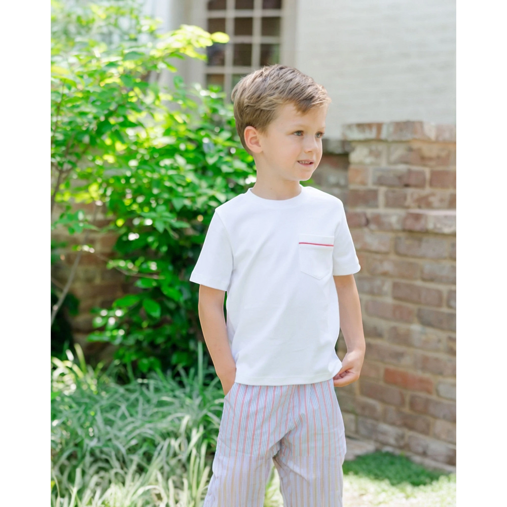 Young boy wearing a white t-shirt with a red stripe and striped pants standing outdoors.